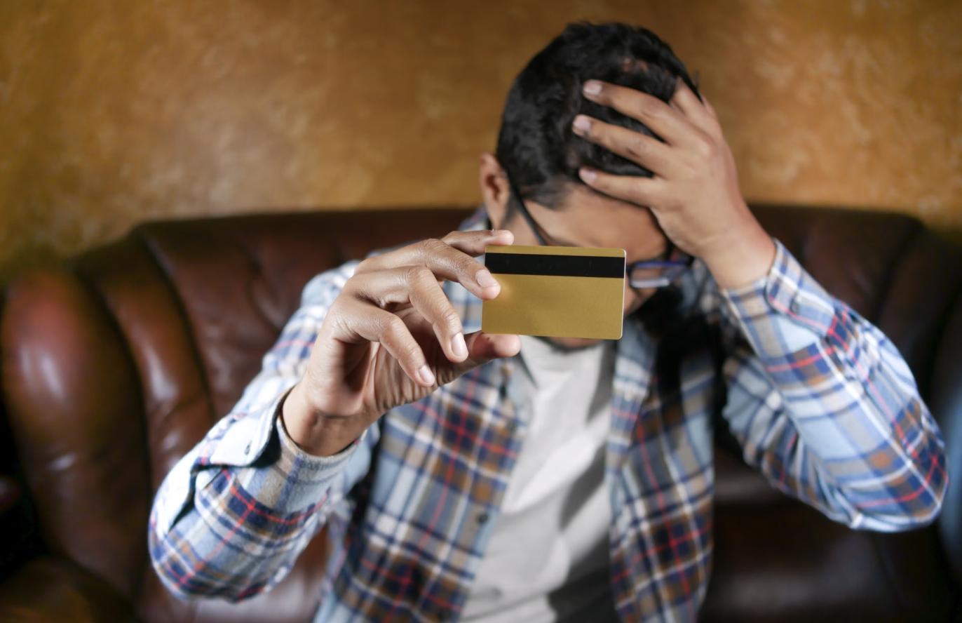 Homme préoccupé qui tient une carte de crédit après avoir utilisé des prêts rapides et des avances d’argent